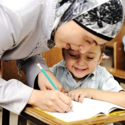 Female Muslim teacher helping a little pupil in the classroom